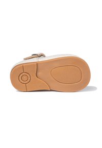 Zapato beige brillante para niños visto desde la suela, con una parte inferior de goma marrón y patrones de acanalado, además de una correa con hebilla.