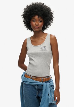 Szary, prążkowany top na ramiączkach z okrągłym dekoltem, z drukowanym logo. Połączony z niebieskimi dżinsami i niebieską koszulą zawiązaną w talii.