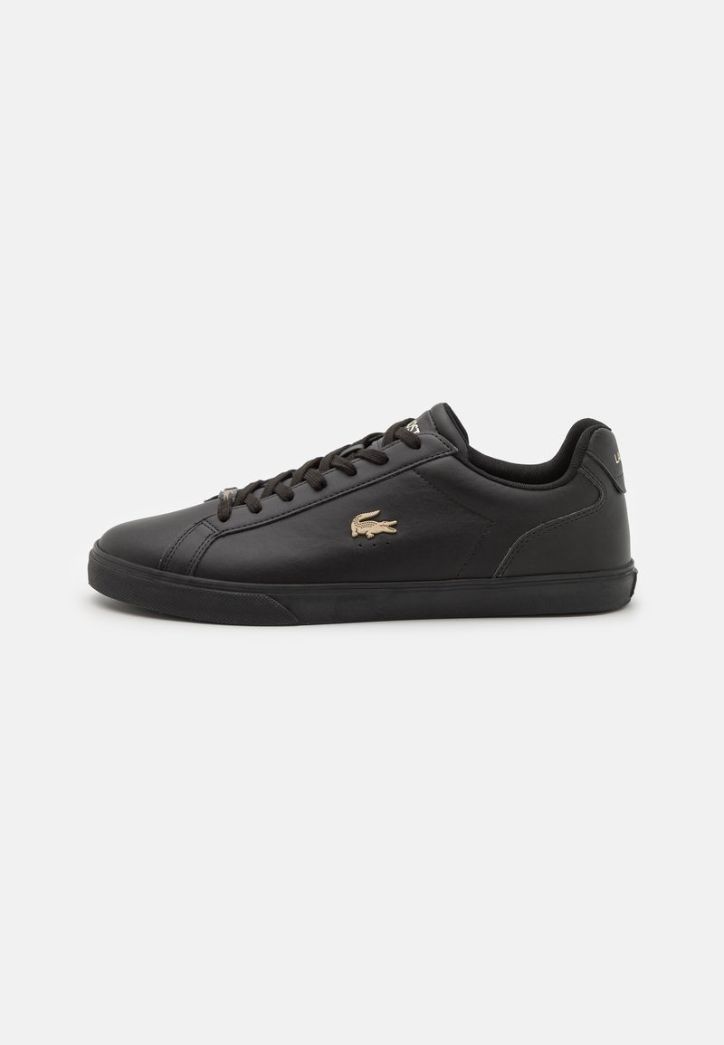 Schwarze Ledersneaker mit einem niedrigen Design, flachen Schnürsenkeln, einer strukturierten Sohle und einem goldenen Logo-Detail an der Seite.