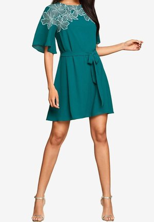 Tyrkysově modré šaty s krátkými rukávy, květinovou výšivkou u výstřihu a detailem zavázání v pase. Vyrobené z lehké látky, plynulá silueta.