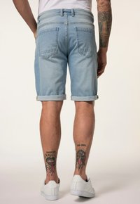 Lyseblå denimshorts med opsmøgte manchetter, der har to baglommer og en klassisk pasform. Hvide sneakers og synlige tatoveringer på benene.