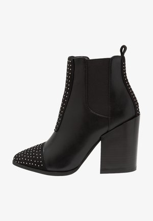 Zwarte enkellaars van leer met een spits toelopende neus, voorzien van gespikkelde accenten en elastische zijpanelen. Dikke blokhak.