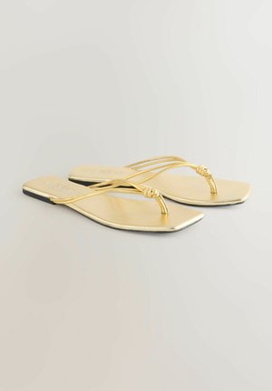 Zeltainas plakanās čības ar gludu apdari, kurām ir plāni krustoti siksniņas un mezgla detaļa starp pirkstiem. Kvadrāta formas zolīte.