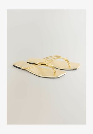 Złote płaskie sandały o gładkim wykończeniu, z cienkimi krzyżującymi się paskami i detalem w postaci węzła między palcami. Kwadratowa podeszwa.