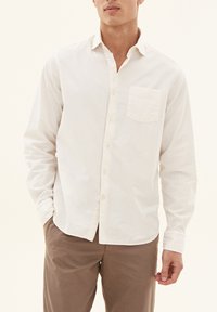 Lys beige skjorte med knaplukning i bomuld, der har en brystlomme, lange ærmer og en klassisk krave. Glat tekstur, skræddersyet pasform.