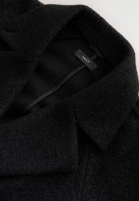Black textured wool coat with wide collar and visible "NEXT" brand label inside neckline.