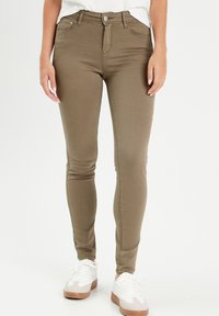 Jeans skinny vert olive à taille haute, avec poches avant et passants de ceinture ; associés à des baskets blanches avec une touche beige.