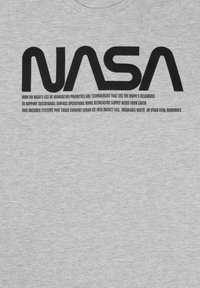 Maglietta grigia con il logo "NASA" in nero al centro. Sotto il logo, del testo nero discute delle tecnologie per le risorse lunari.