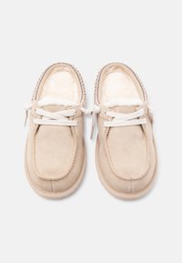 Beige Wildlederschuhe mit weißen Schnürsenkeln und weichem weißem Pelzfutter, von oben auf weißem Hintergrund dargestellt.