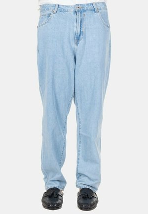 Jeans azzurri chiaro a vita alta indossati con mocassini neri con nappine, mostrati dalla vita ai piedi su uno sfondo uniforme.