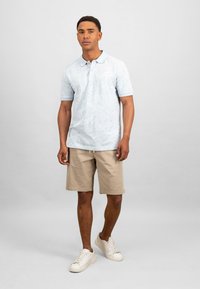 Lyseblå polo skjorte med et subtilt bladmønster, kombinert med beige shorts. Hvite joggesko fullfører antrekket. Enkelt og uformelt design.