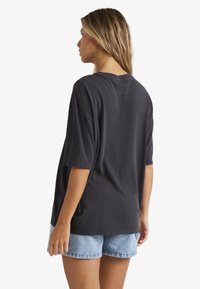 Sort oversized bomulds t-shirt med korte ærmer og rund hals, har en afslappet pasform, vist sammen med lyse denim shorts.