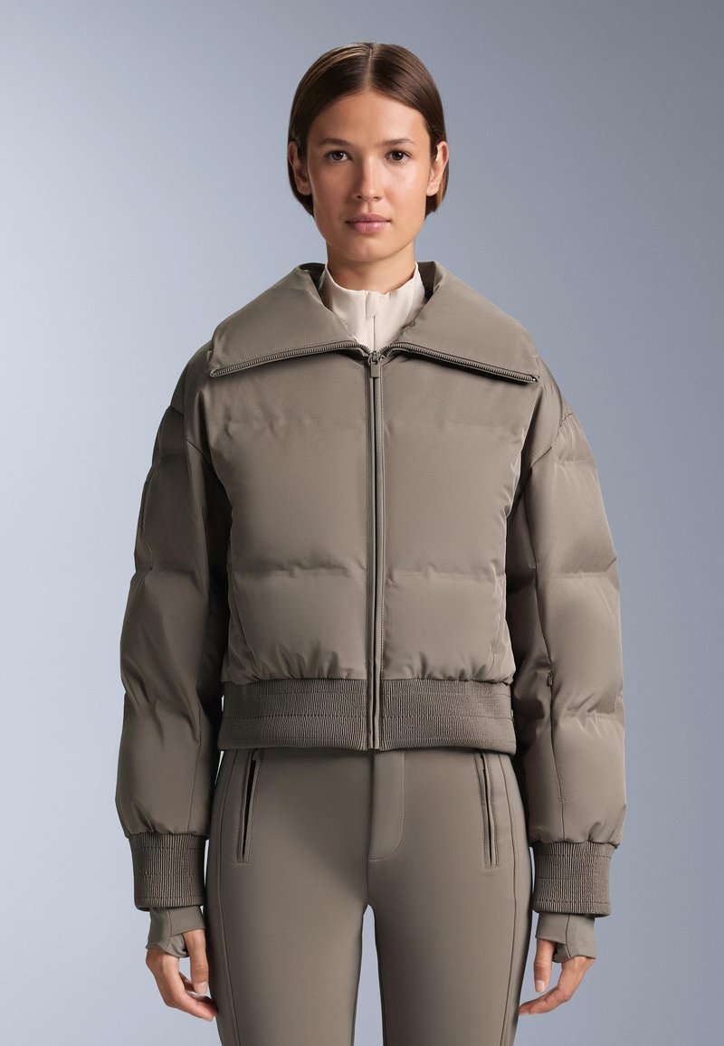 Szürkés tompa árnyalatú, rövidített pufi dzseki, nagy gallérral, elülső cipzárral és bordázott mandzsettával, valamint szegéllyel. Hozzáillő, testhezálló nadrággal párosítva.