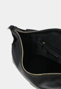 Binnenkant van een zwarte leren handtas met een gladde textuur, gouden rits en een kleine ritszak voorzien van de merknaam.