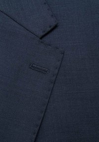 Tessuto blu navy testurizzato che mostra taschini cuciti e un piccolo etichetta, con una finitura liscia e una superficie tessuta uniforme.