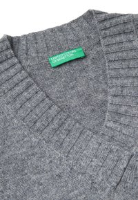 Maglione grigio in lana a collo a V con design a coste sul collo e sulle spalle. L'etichetta riporta "UNITED COLORS OF BENETTON" in verde. Texture morbida.