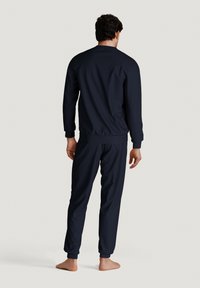Navy athletic tracksuit featuring a zip-up jacket with ribbed cuffs and matching pants with elastic waistband and tapered legs, made from smooth fabric.