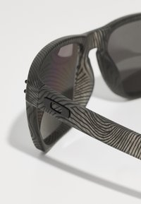 Saulesbrilles ar rakstainu pelēku rāmīti, kurām ir elegants dizains un tumši objektīvi. Melni akcenti izceļ tempļus un eņģu detaļas.