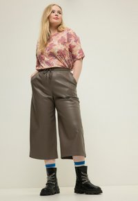 Hnědé kalhoty culottes z umělé kůže s elastickým pasem, spárované s barevným topem s paisley vzorem. Černé bojové boty s řetězovými detaily.
