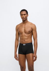 Boxer en coton noir avec une ceinture élastique ornée d'un logo blanc. Texture lisse et design ajusté, porté par un modèle masculin.