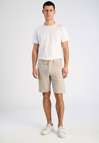 Pantalones cortos rayados de color beige claro con un ajuste holgado, con cierre frontal de botón y dos bolsillos laterales, combinados con una camiseta blanca ajustada.