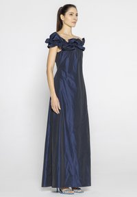 Granatowa satynowa sukienka maxi z dekoltem off-the-shoulder i falbaniastym wykończeniem, o gładkiej fakturze oraz dopasowanej talii, która opada aż do linii hemu.