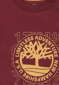 Bordowa koszulka z okrągłym logo drzewa i żółtym napisem. Okrągły dekolt, krótkie rękawy, wykonana z miękkiej bawełny, z grafiką.