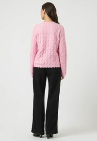 Lyserød tekstureret sweater med lange ærmer, der har en scalloped kant, parret med højtaljede sorte vide bukser og støvler med hæl.