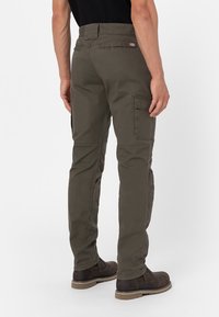 Cargo pants in olive green, featuring multiple pockets, straight leg design, and sturdy fabric. Worn with brown boots.