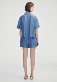 Modrý lehký textilní outfit se zkráceným rukávem, límečkovým topem a odpovídajícími šortkami. Pruhovaná textura, uvolněný střih, minimalistický design.