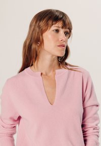 Hellrosa Pullover mit V-Ausschnitt und kurzen Ärmeln, aus weichem Material gefertigt. Verfügt über eine gerippte Textur am Kragen und Saum.