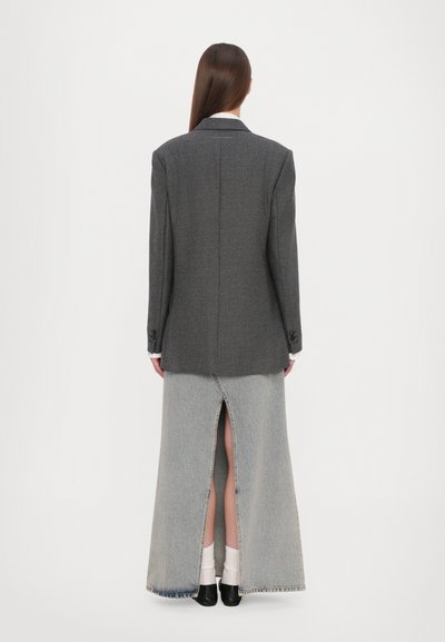 Blazer grigio con una vestibilità su misura, abbinato a una lunga gonna di denim con spacco posteriore. Scarpe nere completano l'outfit.