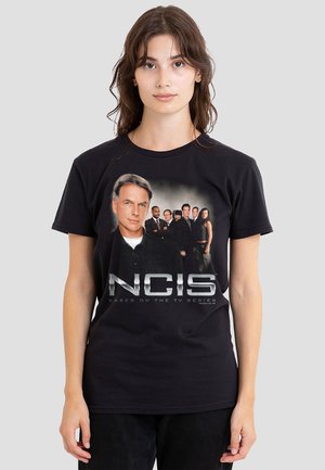 Schwarzes Baumwoll-T-Shirt mit grafischem Druck eines Charakters und Casts aus NCIS. Der Text lautet "NCIS BASIEREND AUF DER TV-SERIE." Klassisches Rundhals-Design.