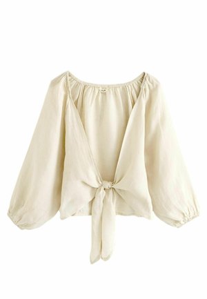 Blouse beige clair avec manches longues bouffantes, col froncé et fermeture à nouer à l'avant. Tissu doux et léger avec une texture lisse.