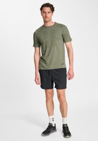 Zielona sportowa koszulka z krótkim rękawem i teksturowanym wzorem, w zestawie z czarnymi szortami i czarnymi trampkami. Charakterystyczne białe skarpetki z wzorem jodełki.