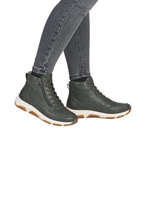 Grüne Leder-High-Top-Sneaker mit Schnürsenkeln und seitlichem Reißverschluss, ausgestattet mit einer weißen Sohle und braunen Akzenten. Getragen mit grauen Skinny-Jeans.