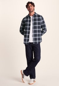 Button-up plaid shirt in dark green, blue, and white, paired with dark denim jeans and white sneakers with black stripes.