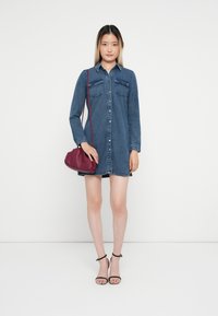 Džinsa kleita ar garām piedurknēm, divām krūšu kabatām, pogu aizdari un saplēstu malām. Valkāta ar bordo krāsas crossbody somu un melniem papēžiem.