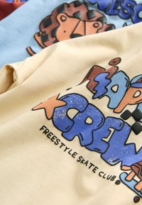 Deux sweat-shirts pliés, un beige et un bleu clair, avec un texte graffiti coloré et un dessin de lion cartoon.