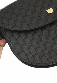 Borsa a tracolla in pelle intrecciata nera con pattina curvata e delicati dettagli in oro. Finitura testurizzata, design compatto e bordi arrotondati.