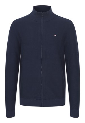 Jūras spēku tumši zils džemperis ar rāvējslēdzēju, izgatavots no ribotā adījuma auduma. Tam ir pacelta apkakle, garas piedurknes un neliels logo sarkanā, baltā un zilā krāsā uz krūšu daļas.