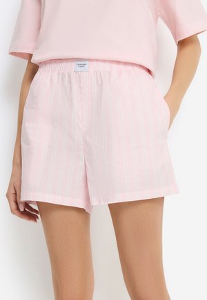 Light pink striped shorts with elastic waistband and front label worn with matching pink top, model's hands resting at sides.