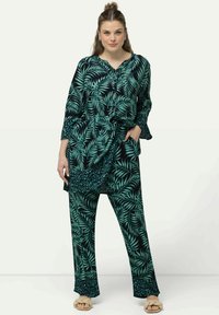 Smaragdgrön och svart outfit med en lös tunika med knappslå och vida byxor, båda med löviga mönster.