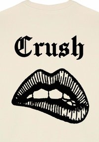 Beige színű pulóver, amelyen fekete grafika található nyitott ajkakról, látható fogakkal, felette a "Crush" szó vastag, gótikus stílusú betűkkel.