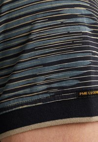 T-shirt à manches courtes marine avec des rayures horizontales bleu et beige, présentant une texture en tricot douce et une étiquette "PME LEGEND" sur l'ourlet.