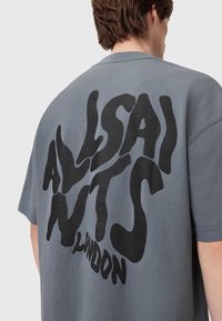 T-shirt de algodão cinza com um grande gráfico de logotipo preto nas costas, com um ajuste relaxado e mangas curtas.