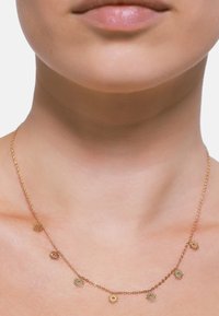 Goldene Halskette mit einer zarten Kette, die kleine, gleichmäßig verteilte, sonnenscheinartige Anhänger aufweist. Glatte Textur, minimalistisches Design.