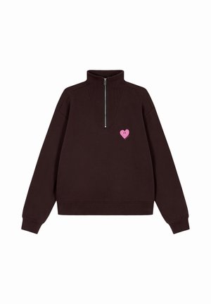 Bruine sweater met een hoge kraag en een zilveren rits. Heeft een roze hartgrafiek op de borst. Zachte textuur en een relaxed pasvorm.