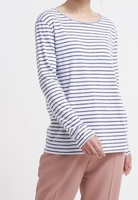 Maglietta a maniche lunghe con collo rotondo, a righe orizzontali bianche e blu navy. Tessuto morbido con vestibilità comoda. Indossata con pantaloni rosa chiaro.