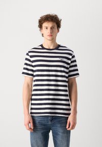 Navy- und weiß gestreites Baumwoll-T-Shirt mit Rundhalsausschnitt, kurzen Ärmeln und kleinem Logo auf der Brust, kombiniert mit blauen Jeans.